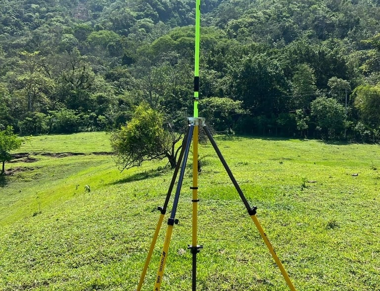 Professional GPS surveying equipment on a tripod in a grassy field with lush green mountains.