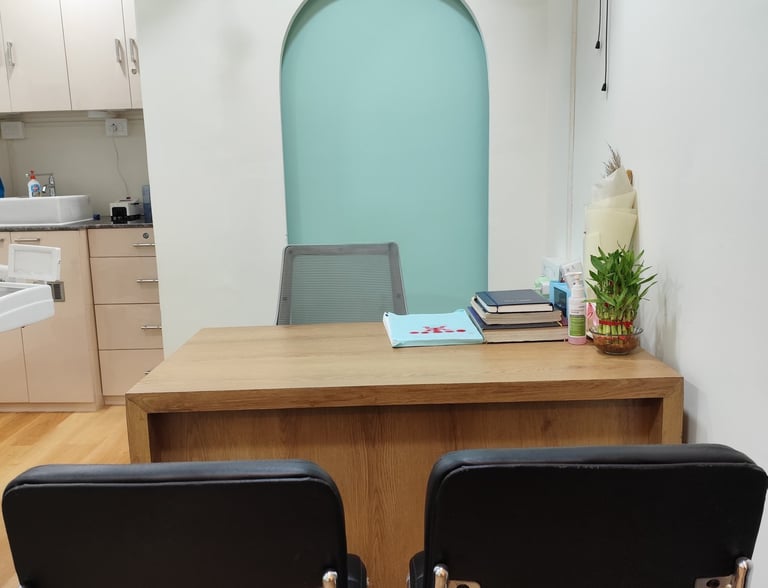 Modern medical consultation office with a wooden desk, black patient chairs, and teal arched wall niche.