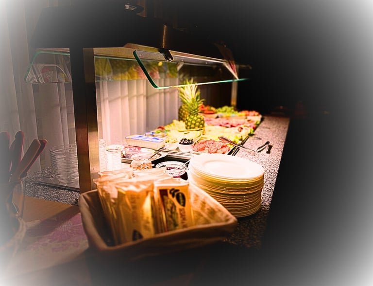 Hotel breakfast buffet featuring fresh pineapple, deli meats, cheese, and stacks of plates.