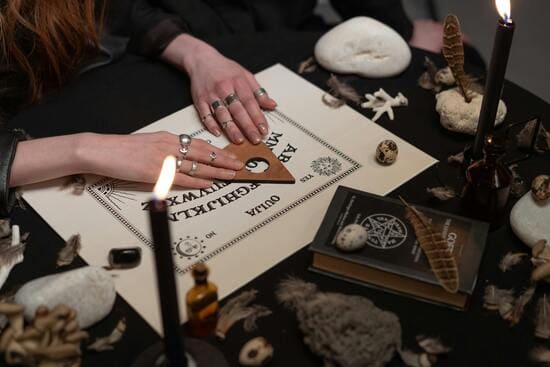 Manos sobre una tabla ouija en una sesión espiritual iluminada por velas.