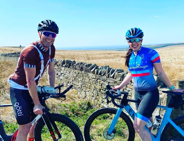 Two smiling road cyclists in gear posing with their bikes on a scenic countryside route.