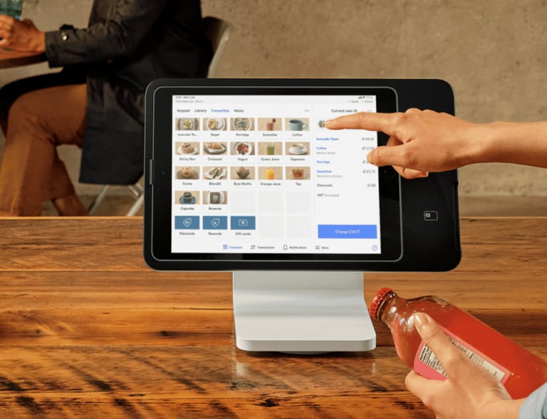 A person uses a digital tablet POS system on a wooden counter to process a retail transaction.