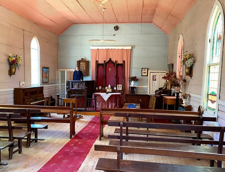 Interior of our historic wooden church with rows of pews, a red aisle carpet, and a simple altar.