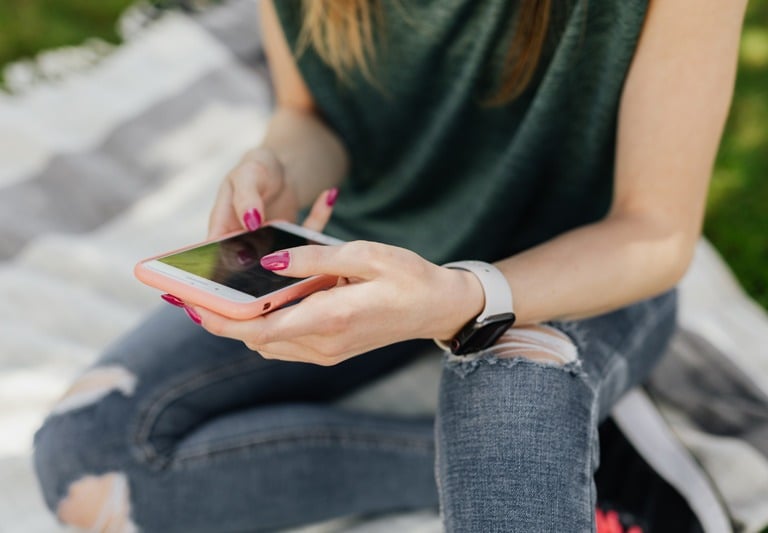Photo of an adolescent girl with ripped jeans using a smartphone