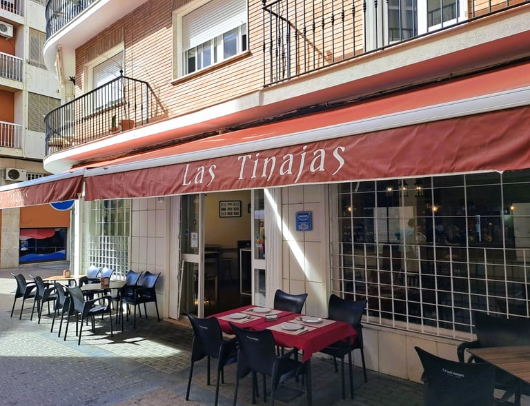Historia del Bar Las Tinajas Huelva reflejada en su fachada exterior y terraza, con mesas listas para recibir a los clientes.