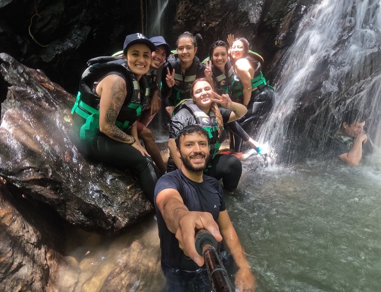 Un grupo de viajeros felices con chalecos salvavidas se toma una selfie bajo una cascada tropical 