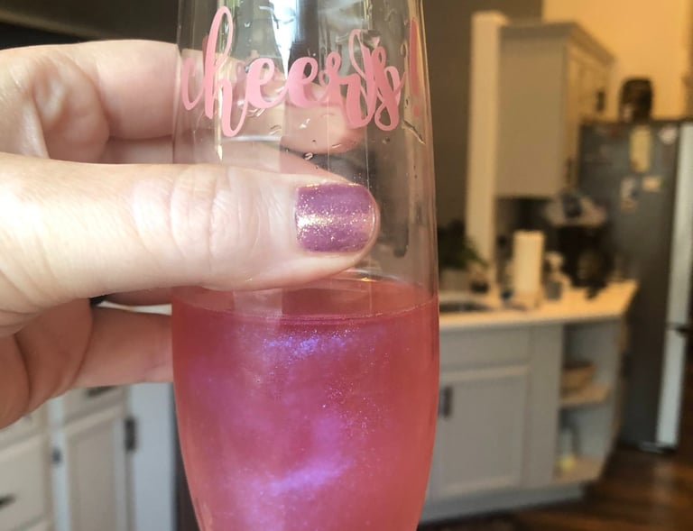 a person holding a wine glass with a pink edible glitter in their drink