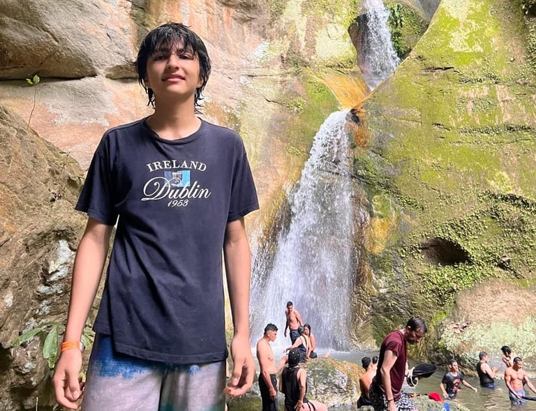 Un joven viajera posando frente a una majestuosa cascada escalonada que fluye sobre acantilados 