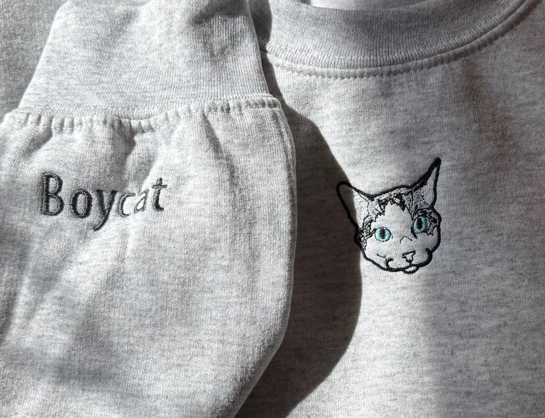 a light gray sweatshirt with a picture of a cat embroidered on it