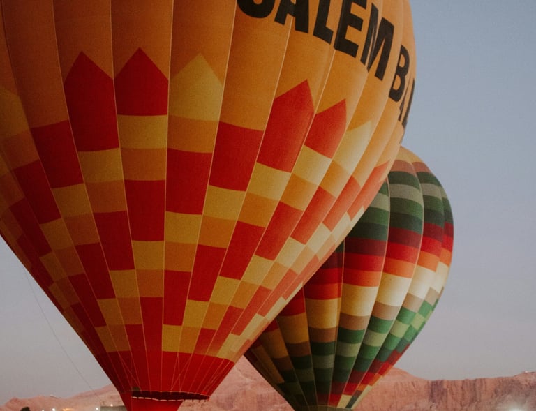 Two colorful hot air balloons floating over the Egyptian desert landscape.
