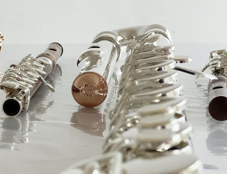 une flûte traversière en or, un piccolo en bois et une flûte en sol en argent, posées côte à côte