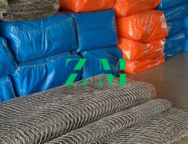 Rolls of flexible stainless steel wire rope mesh near blue and orange industrial packaging bags.