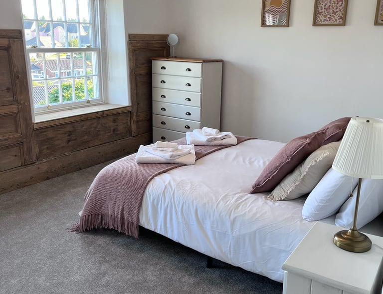 Completed bedroom with neutral tones, layered bedding, and restored woodwork.