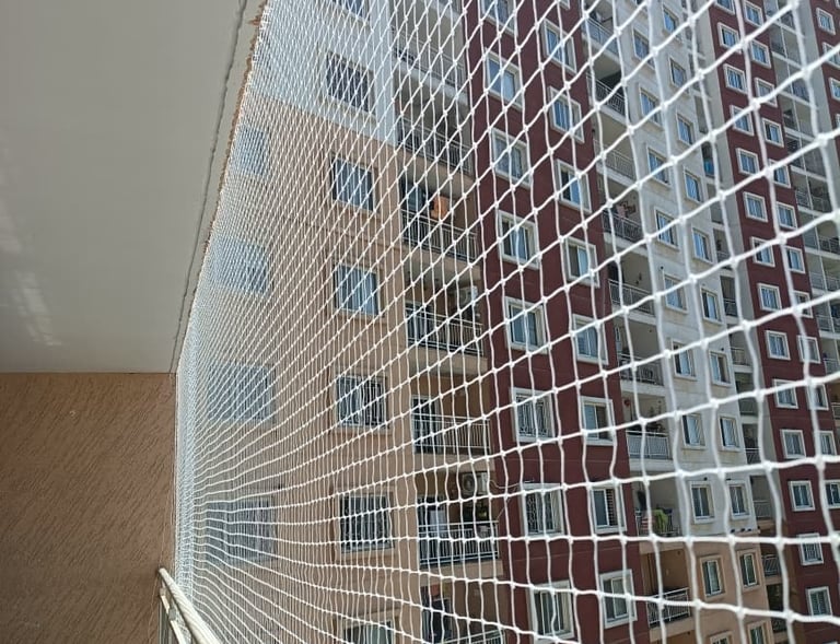 Wide shot of a high-rise balcony fitted with a durable pigeon safety net under bright daylight.