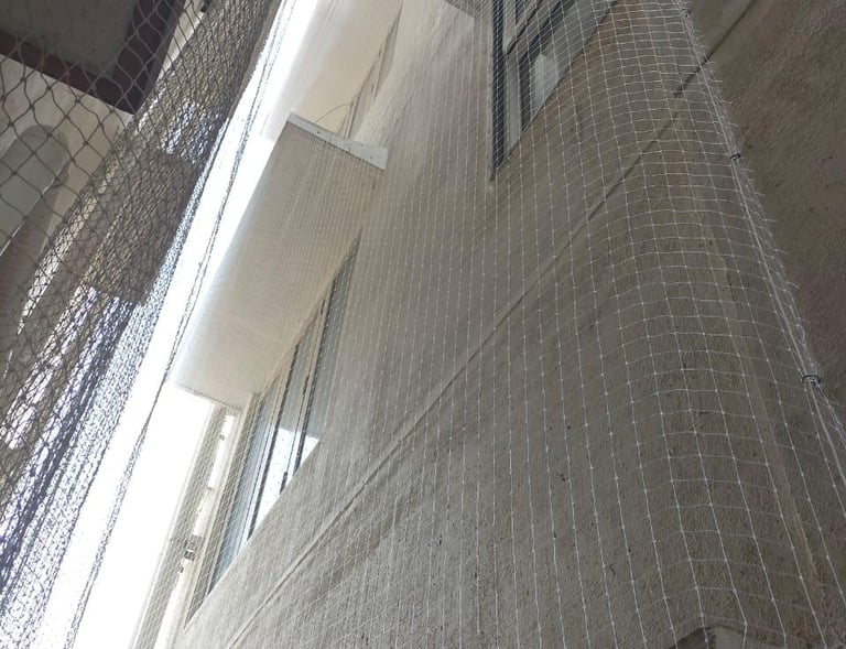 Installation team securing anti-pigeon nets around duct openings in a residential building.
