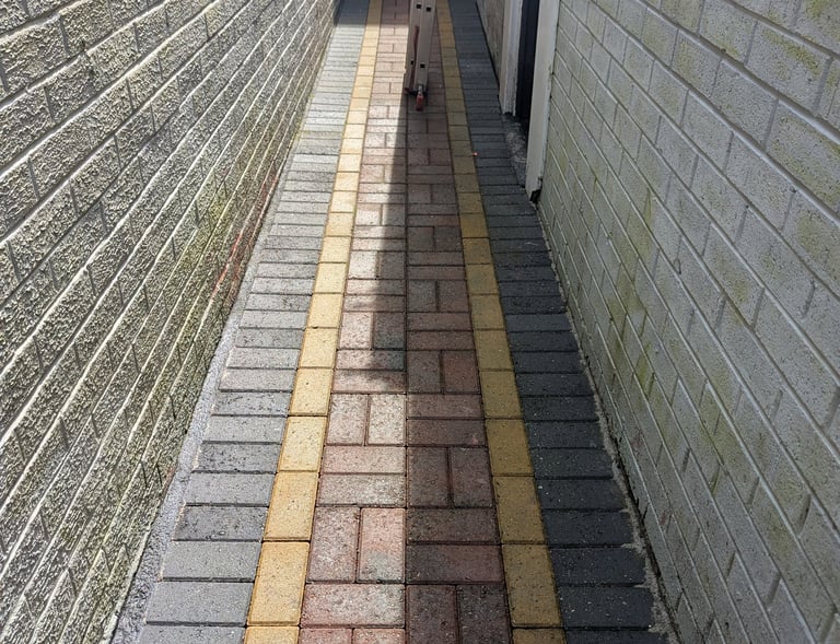 After alleyway featuring multi-colored block paving stones between two light-colored brick walls.