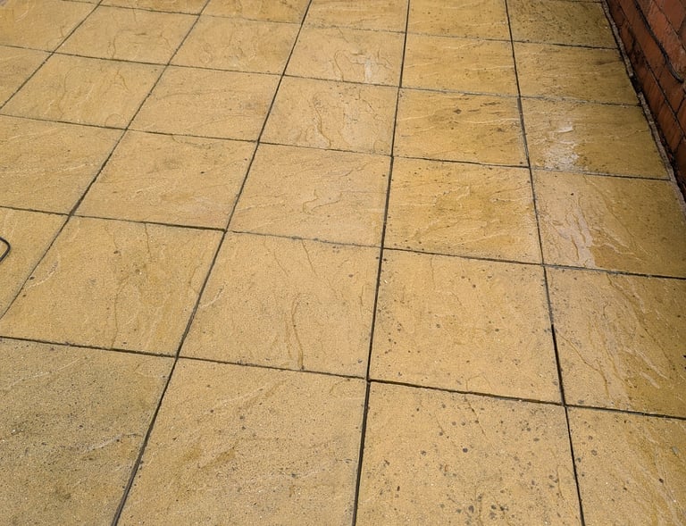After yellow patio paving slabs next to a red brick wall, showing the need for patio cleaning.