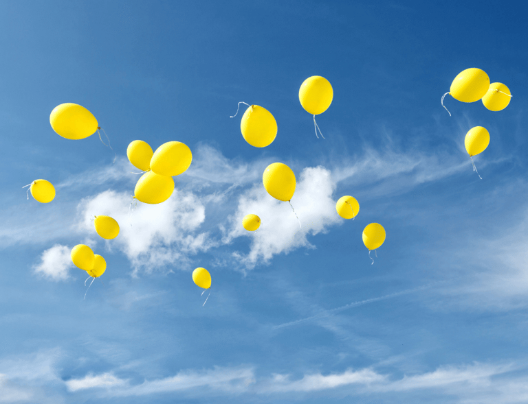 Cielo azzurro limpido con palloncini gialli che volano via, simbolo del lasciare andare, di libertà