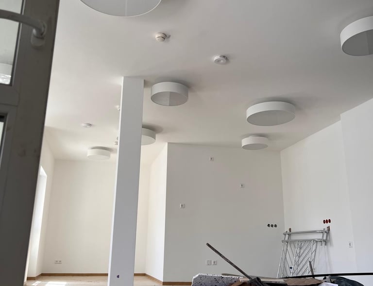 ein großer, weißeer, sanierter Raum mit künstlerischen Trockenbauelementen an der Decke