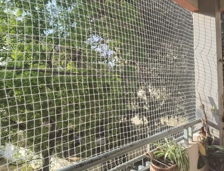 Installation team working together to secure a large safety net on a high-rise balcony.