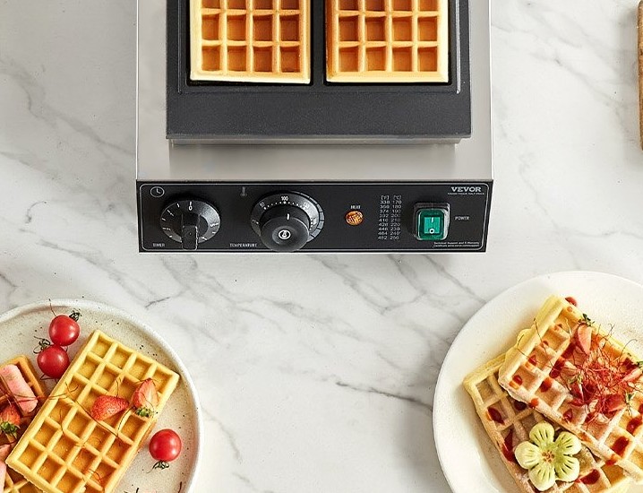 Professional commercial waffle maker with freshly baked golden waffles on plates.