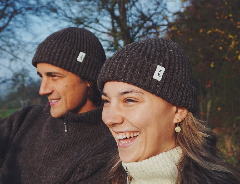 zwei Personen tragen jeweils eine Mütze in dunkeler Farbe mit dem Logo "piies"