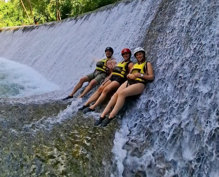 three people sitting on a waterfall in a jungle