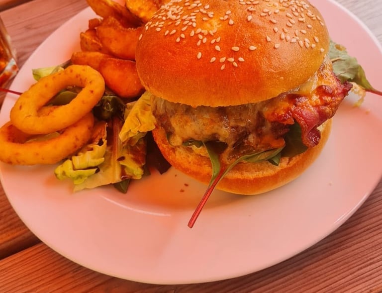 Gourmet bacon cheeseburger Black angus on a sesame seed bun served with wedges and onion rings.