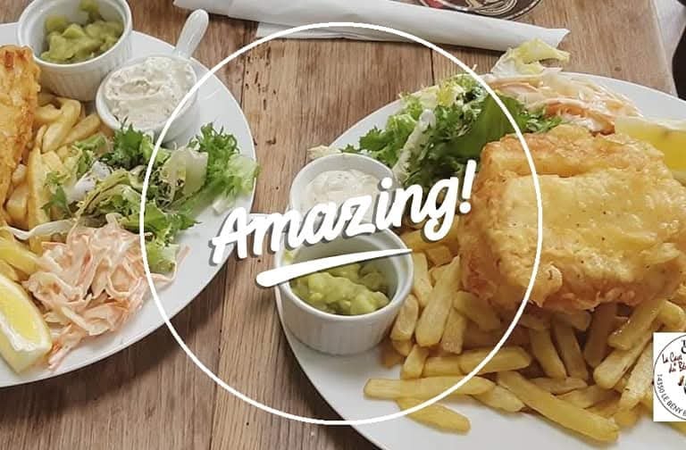 Crispy battered fish and chips served with mushy peas, tartar sauce, and side salad on a wooden table.