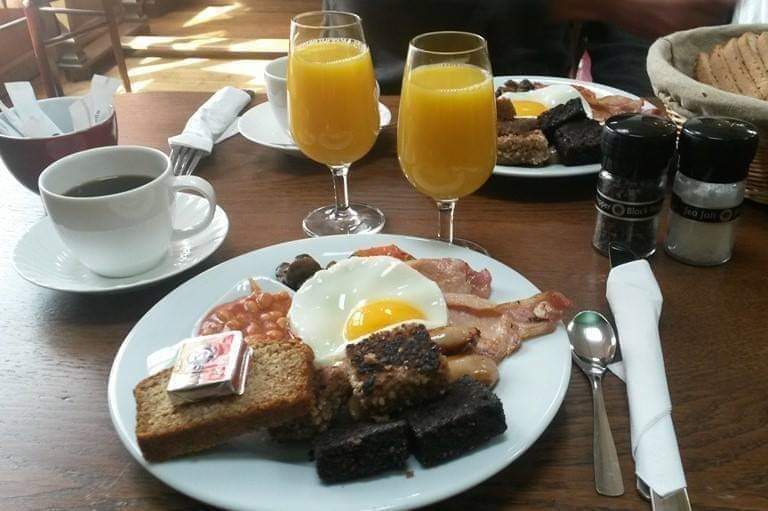 Full Irish breakfast plate with fried egg, black pudding, soda bread, coffee, and orange juice.