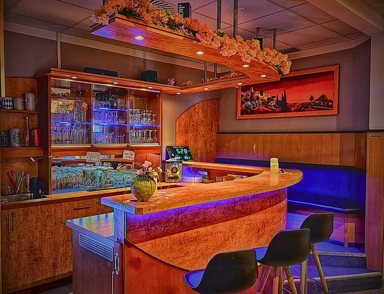 Modern wooden bar counter with colorful LED lighting, floral accents, and bar stools.