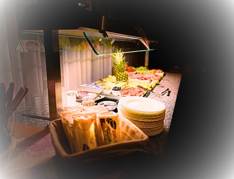 Hotel breakfast buffet featuring fresh pineapple, deli meats, cheese, and stacks of plates.