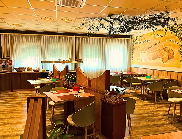 Cozy hotel breakfast room with wooden tables, cafe mural, and buffet area.