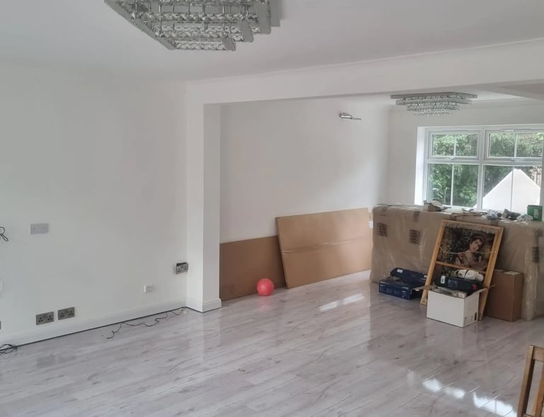 Modern living room with white walls, grey wood laminate flooring, and elegant crystal chandelier lighting.