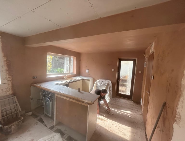 A professional plasterer applying finishing touches to fresh plaster walls in a kitchen renovation.