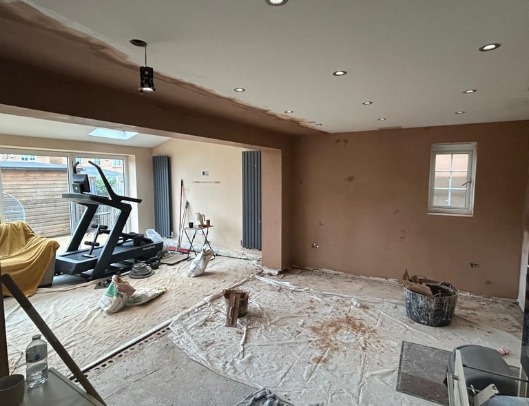 A room undergoing home renovation with freshly plastered walls and a treadmill on dust sheets.