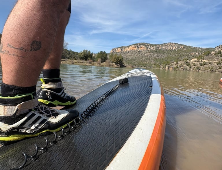 Primer plano de una persona sobre la tabla de paddle surf con grandes montañas al fondo