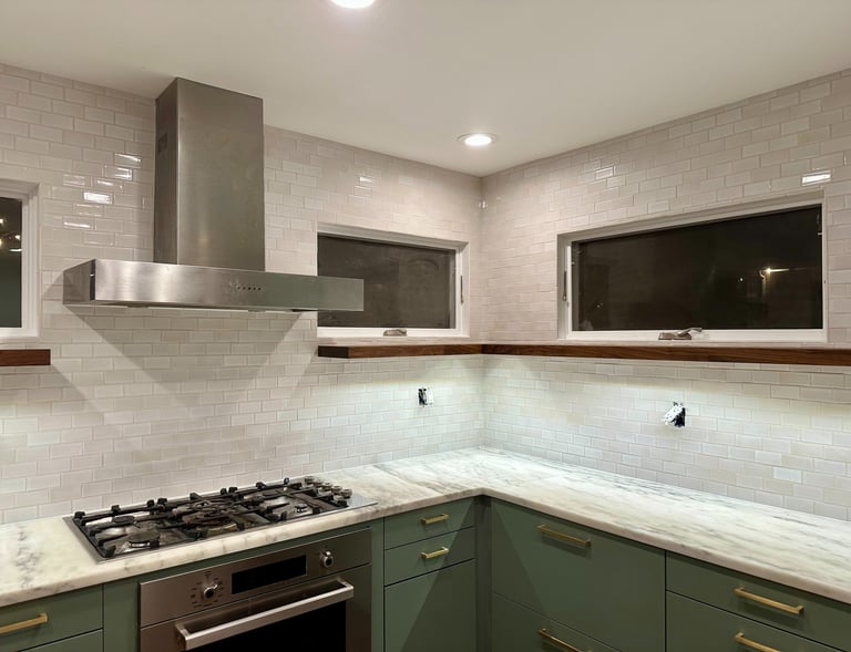 Modern kitchen with white subway tile backsplash, green cabinets, and stainless steel range hood.