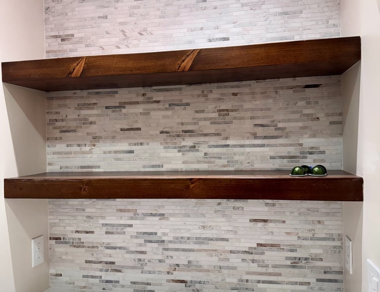 Rustic dark wood floating shelves mounted on a light grey stone mosaic tile backsplash.