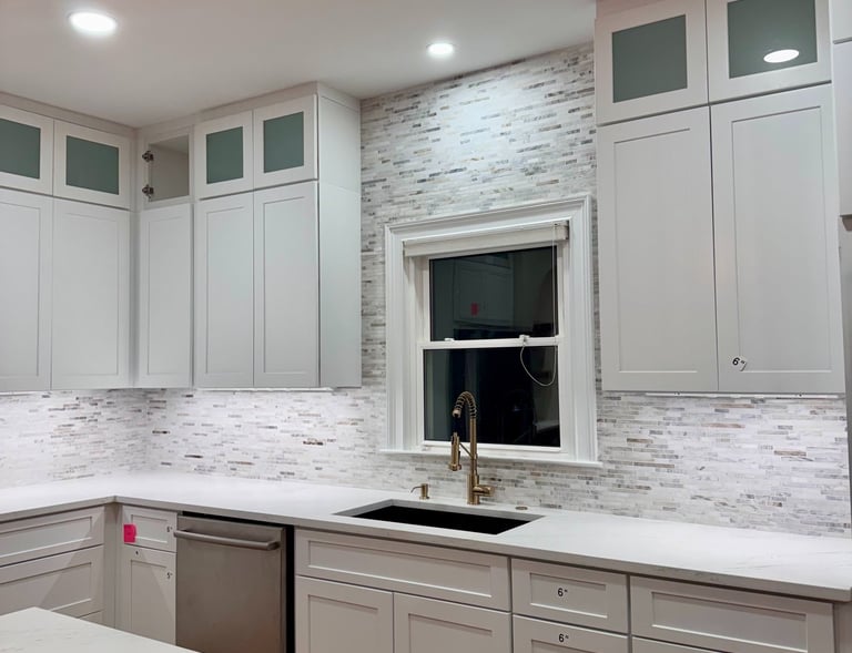 Modern white kitchen with shaker cabinets, gold faucet, and stone tile backsplash.