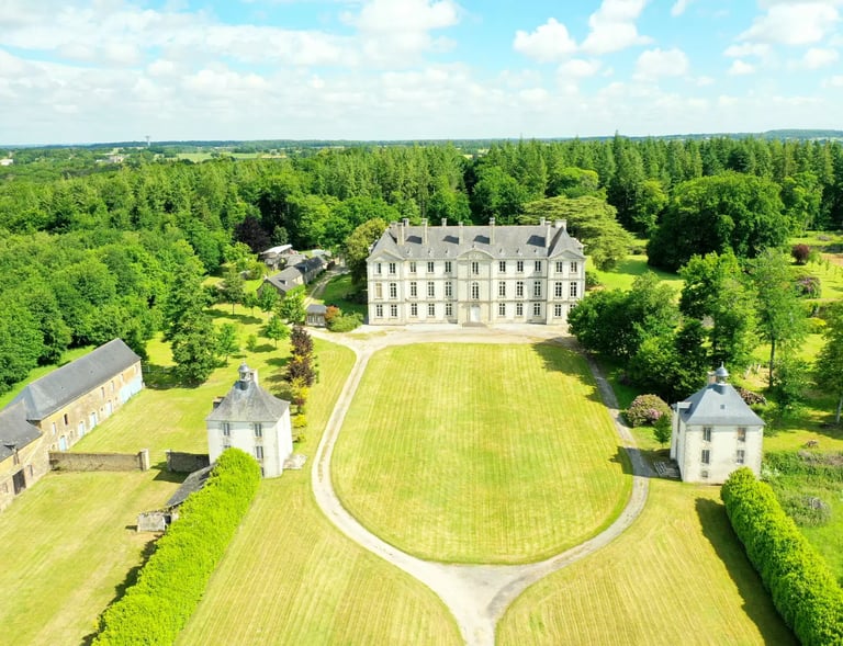 Vue aérienne d'un château français historique avec une grande pelouse et une forêt verdoyante luxuri