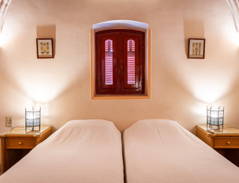 villa bedroom featuring twin beds, ornate metal lanterns, and a red arched window shutter.