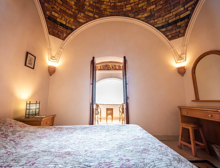 Rustic bedroom with a vaulted brick ceiling, wooden vanity, and balcony view.