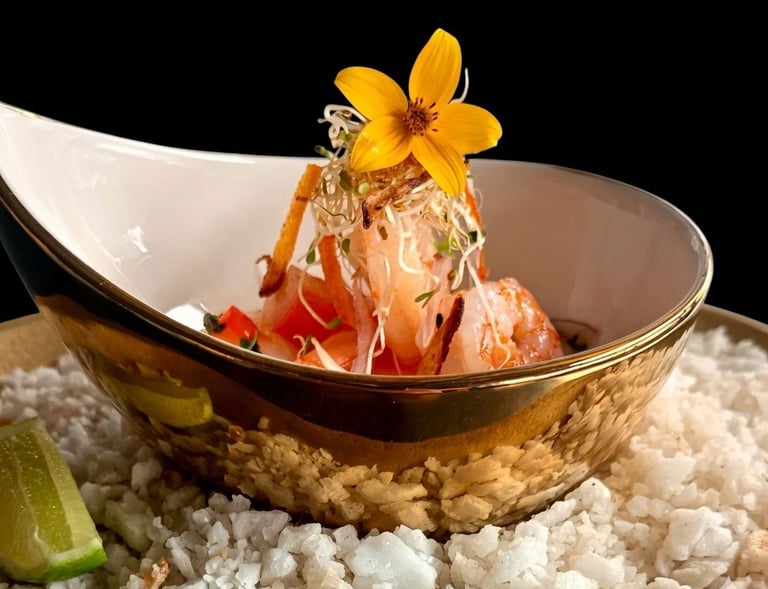 Gourmet shrimp ceviche appetizer served in a gold bowl with edible flowers and sprouts over sea salt.