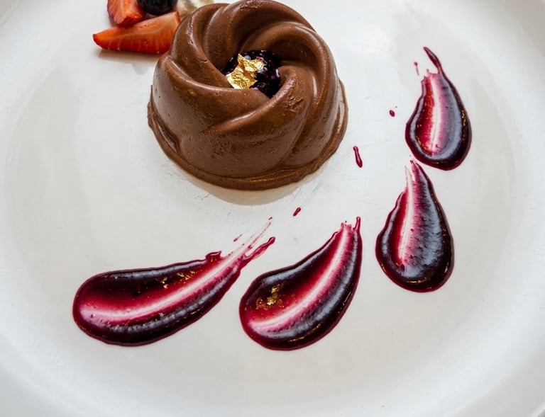 Gourmet chocolate mousse dessert with berry coulis, fresh strawberries, and gold leaf garnish on a white plate.