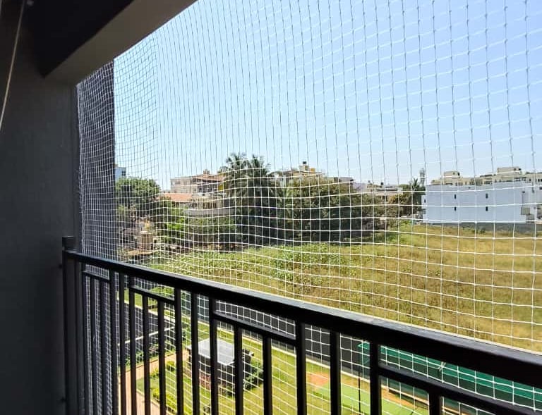 A cozy balcony enclosed with safety nets, plants thriving inside, showing a safe and green space.