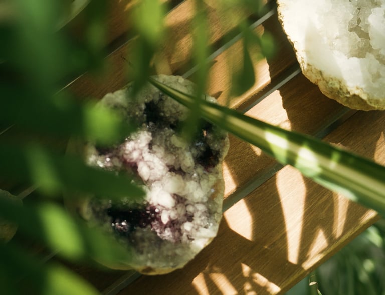 Weiße Kristallgeode mit violetten Akzenten auf Holz, umgeben von grünen Blättern.