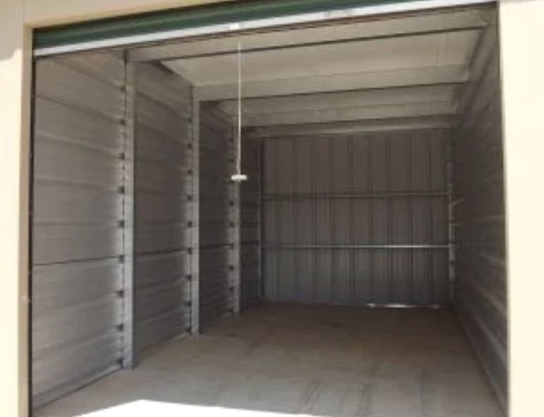 An open, 10X20 foot empty self-storage unit with clean metal walls and a roll-up door.