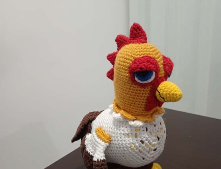Handmade crochet amigurumi chicken toy inspired by Stardew Valley standing on a dark wooden table.