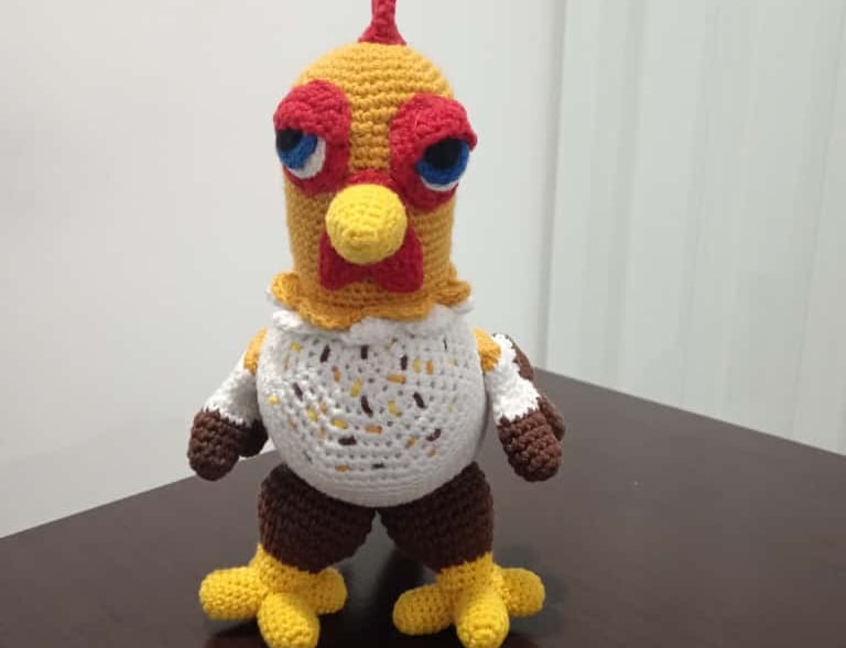 Handmade crochet amigurumi chicken plush toy standing on a dark wooden table.